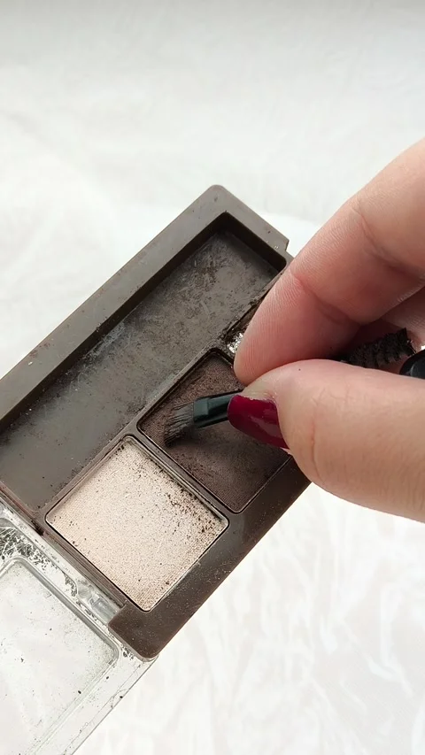 A womans hand uses a brush to take brown eye shadow from a palette with brown 動画素材 314306955