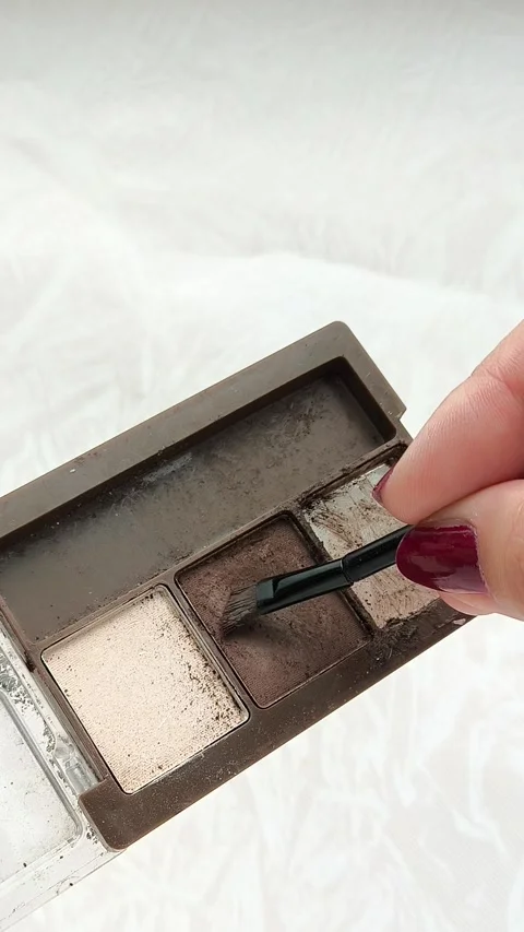 A womans hand uses a brush to take brown eye shadow from a palette with brown Stock Footage 314306995