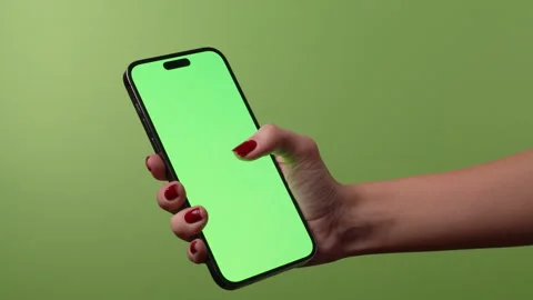 A womans hand uses an iPhone with a green screen background and green display Stock Footage 321262957