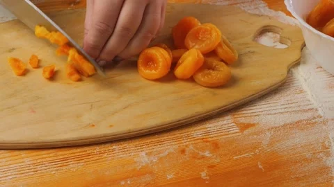 A woman's hand uses a knife to cut dried apricots on a wooden board. Medium.. Vidéo 272663718