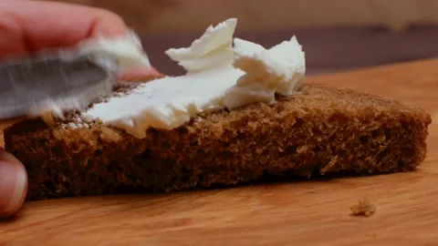 Woman's hand uses a knife to spread butter on the ruddy half of a slice of bread Stock Footage 150836499