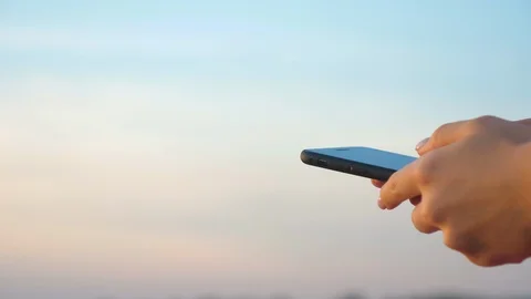 Woman's hand using mobile phone with a clear sky in the background. Stock-Footage 115981129