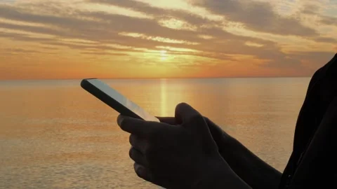 Woman's hand using mobile phone by the sea at sunset. Stock Footage 310498500