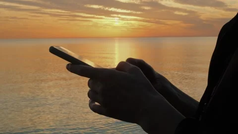 Woman's hand using mobile phone by the sea at sunset. Stock Footage 312907238