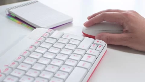 Woman's hand using mouse next to a white keyboard, notepad on white desk. Stock Footage 136216507