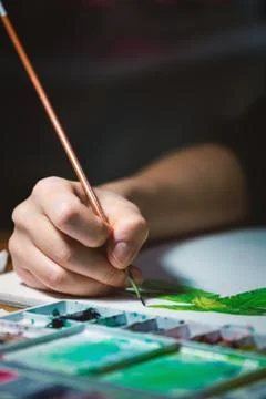 Woman's hand using small brush to paint picture on white paper Stock Photos