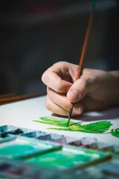 Woman's hand using small brush to paint picture on white paper Stock Photos