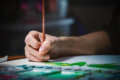 Woman's hand using small brush to paint picture on white paper Stock Photos