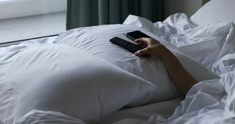 Woman's hand using TV remote control and smartphone on bed in the morning Video stock 112241845