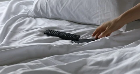 Woman's hand using TV remote control and smartphone on bed in the morning Video stock 112245091