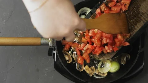 A woman's hand will drop tomatoes chopped on a board into a pan with onions and Stock Footage 170449318