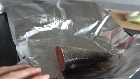 A woman's hand wraps a piece of red fish in foil before baking it in the oven. Stock Footage 336594887