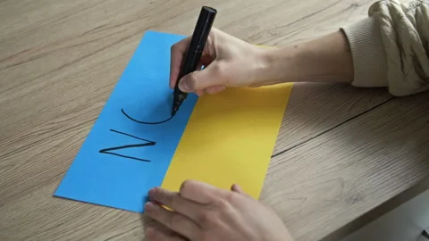 Woman's hand writes on the background of the Ukrainian Flag NO WAR. Stock Footage 170957864