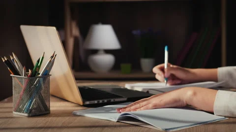 A woman's hand writes in a notebook, sitting near a laptop at home Stock Footage 136085079