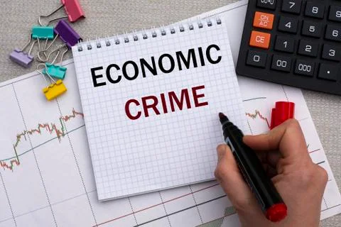 A woman's hand writes in a notebook the words ECONOMIC CRIME on the backgroun Stock Photos