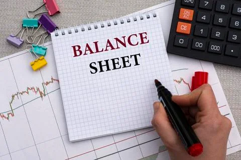 A woman's hand writes in a notebook the words BALANCE SHEET on the background Stock Photos