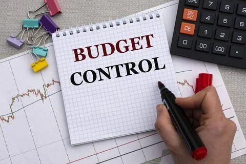 A woman's hand writes in a notebook the words BUDGET CONTROL on the backgroun Stock Photos