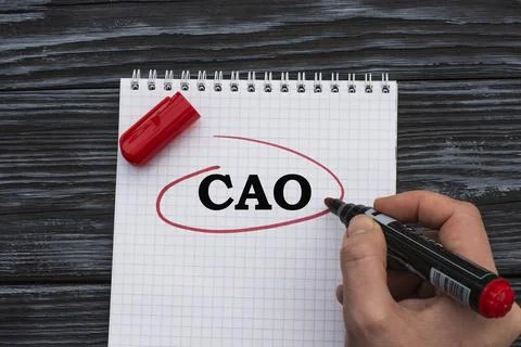 A woman's hand writes on a white sheet the word CAO on a black wooden backgro Stock Photos
