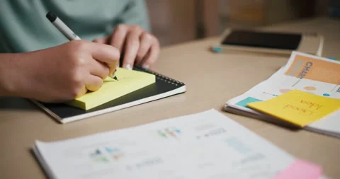 A woman's hand is writing a message on a sticky note on desk. Vidéo 313868226