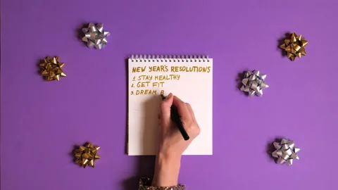 Woman's hand writing new years resolutions in textbook on violet background. Stock Footage
