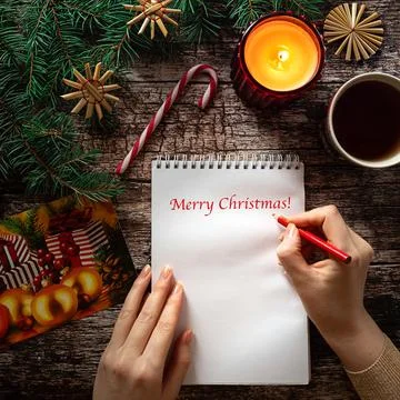 Woman's hand writing on a notepad sheet in Christmas setting Stock Photos