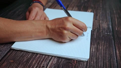 A woman's hand writing with a pen in a notebook on a wooden table, close-up Stock Footage 243293373