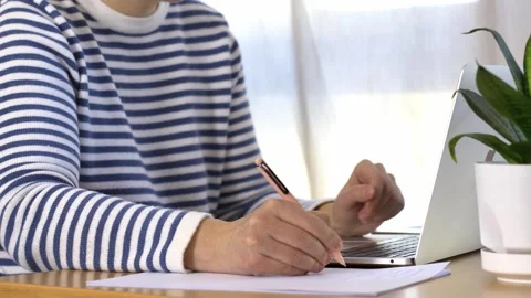 A woman’s hand writing with a pen while working on a laptop Stock Footage 304668707