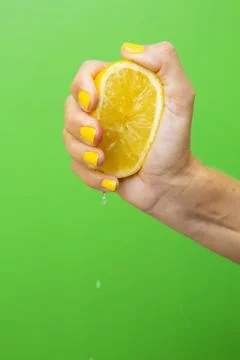 A woman's hand with yellow fingernails squeezing half a lemon. Stock Photos