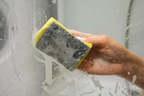 A woman's hand with a yellow sponge washes the glass in the shower stall Stock Photos