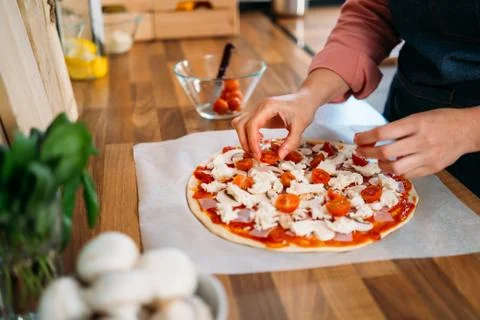 Woman's hands adding cherry tomatoes to a traditional margarita pizza. Prepar Stock Photos