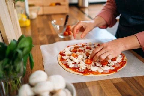 Woman's hands adding cherry tomatoes to a traditional margarita pizza. Prepar Stock Photos