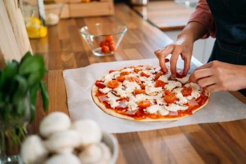 Woman's hands adding cherry tomatoes to a traditional margarita pizza. Prepar Stock Photos