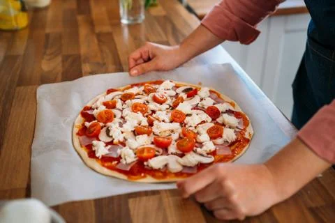 Woman's hands adding cherry tomatoes to a traditional margarita pizza. Prepar Stock Photos