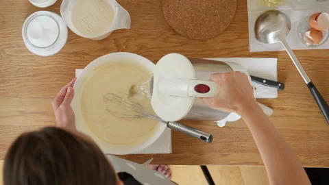 Woman's hands adding hot water from a kettle to thin pancake batter, top view Stock Footage 315358418