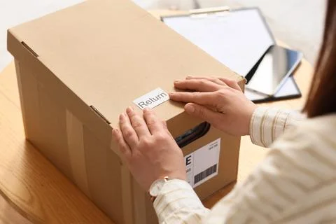 Womans hands applying a return label to a cardboard box for shipping, e-comme Stock Photos