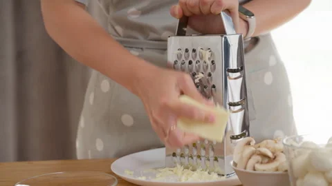 A woman's hands are grating a block of mozzarella cheese on a metal grater Stock Footage 315670762
