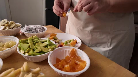 Womans hands are making fruit kebabs, stringing pieces of fruit on a skewer Stock Footage 329940269