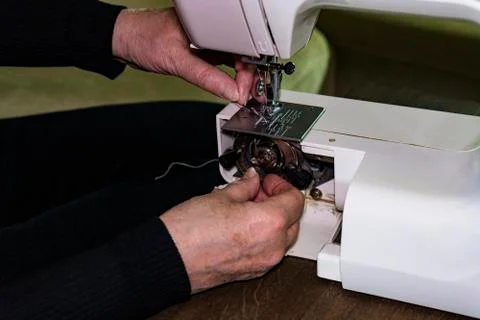 The woman's hands are replacing the spool of thread in the sewing machine. Stock Photos