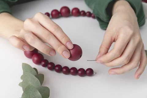 Womans hands are stringing red colored beads on a wire. Close up Stock Photos