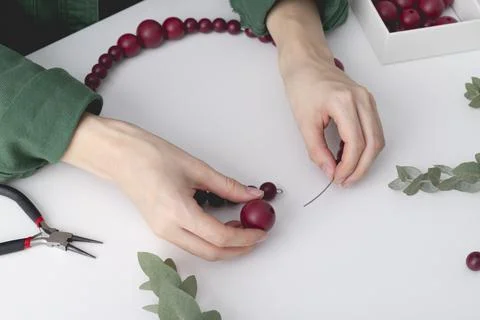 Womans hands are stringing red colored beads on a wire. Stock Photos