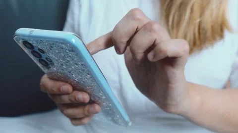 Woman's hands browsing content on a mobile phone displaying a light blue Stock Footage 335151582