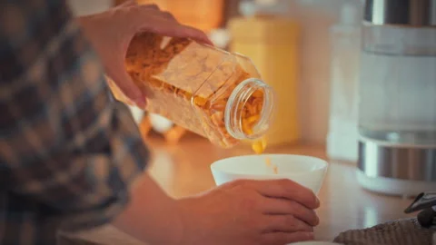 A womans hands carefully pour yellow cornflakes into a white bowl preparing Stock Footage 335125002
