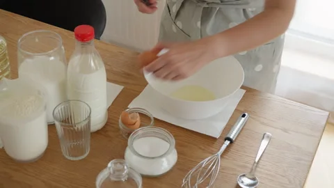 Woman's hands cracking a fresh brown egg into a white bowl for cooking dough Stock Footage 315357898