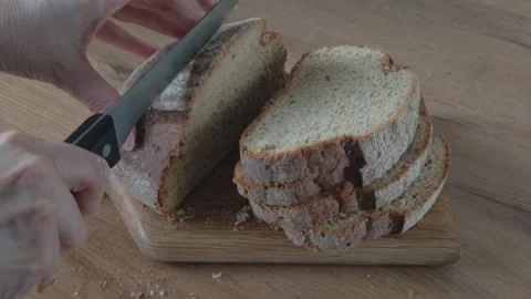 Woman's hands cut bread with a black-handled knife on a wooden cutting boar.. Stock Footage 339018370