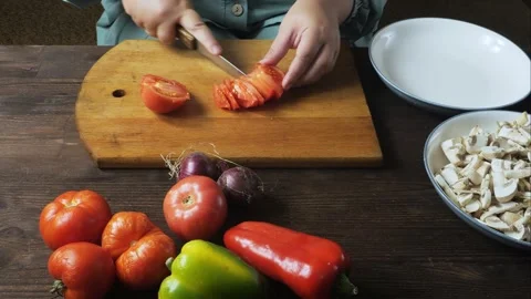 A woman's hands cut fresh red tomatoes with a knife on a cutting board on a.. Stock-Footage 332734699