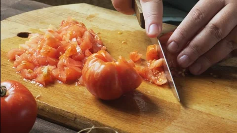 A woman's hands cut fresh tomatoes with a knife on a cutting board on a woo.. Vidéo 330215152