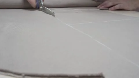 Woman's hands cutting a beige fabric with scissors on table in atelier Stock Footage 157812331