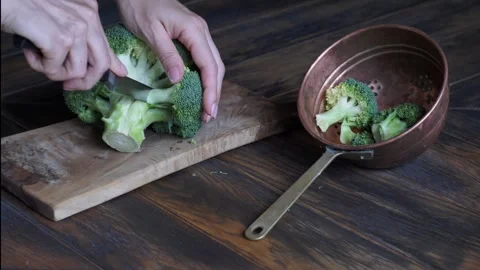 Woman's hands cutting broccoli cabbage on cutting board with small knife Stock Footage 247729379