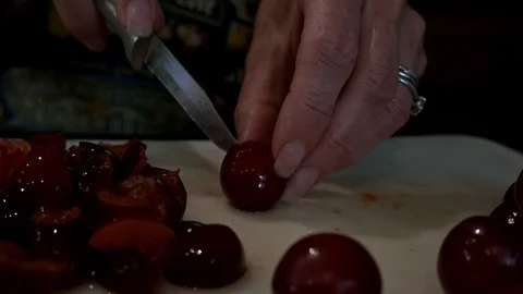 Woman's hands cutting plums in half with knife on chopping board. Stock Footage 111868316