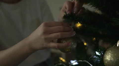 Woman's hands decorating a christmas tree with golden baubles Stock Footage 317506932